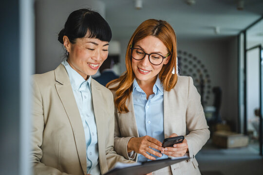 two diverse female colleagues review together document files in hallway