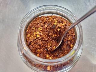 Chili flakes in a jar with a spoon, ready to be used as a condiment.