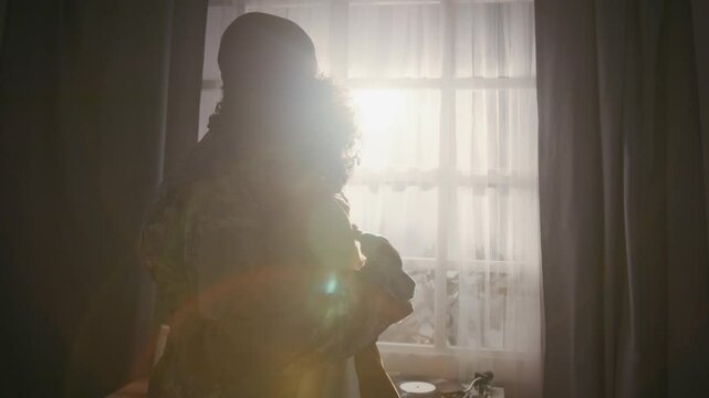 Medium shot with lens flare of African American marine father in khaki military uniform and teenage son clasping hands then hugging while saying goodbye before departing on mission