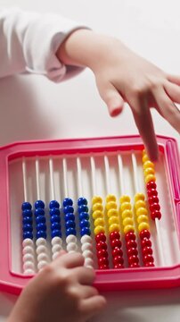Cute little schoolgirl does sums moving plastic beads by left hand finger on colorful abacus at arithmetic lesson at home upper closeup slow motion