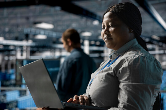 Teamworking data center programmers writing code for resource optimization using notebook. Server farm coworkers in data center refining algorithms for faster processing using laptop