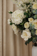 Elegant white flowers with green eucalyptus in a white vase, set against beige patterned curtains. Neutral tones. Suitable for wedding, celebration, luxury decor, floral arrangement concepts.