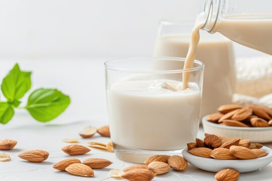 Pouring almond milk into glass with almonds and basil leaves