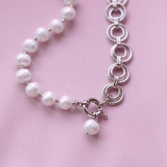 Close-up of elegant bracelet with white pearls and textured silver links on pink satin fabric. Jewelry detail for fashion, femininity, elegance, and gift concepts. Luxury and beauty theme.