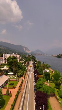 Drone video of charming towns on Lake Maggiore, Italy, including Stresa and Verbania, with historic grand hotels, sunlit roads, and vibrant lakeside life under bright midday sun