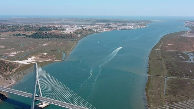 Panoramic aerial view capturing international bridge spanning guadiana river, with sailing boat navigating near ayamonte city under bright sunlight in andalusian landscape