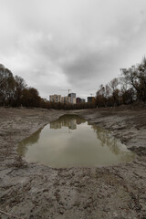 Empty lake with stagnant water and residential buildings under cloudy sky.