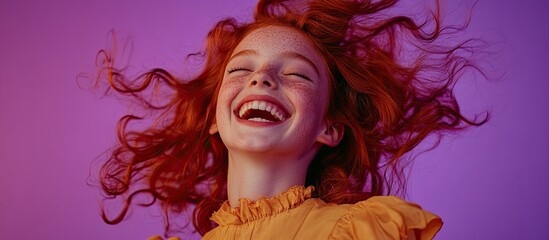 A beautiful girl with red hair laughing and smiling, her head tilted back as she holds up her windblown hair against a purple background