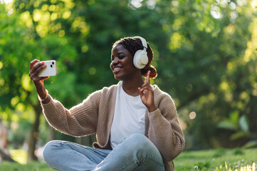 Young woman taking selfie while listening music with headphones in park