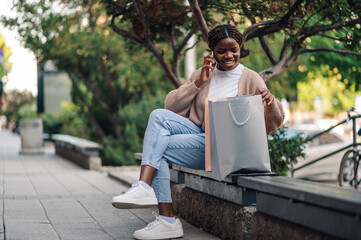 Happy shopper checking bags while talking on phone on bench