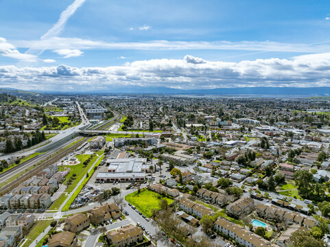 Drone images showcasing residential neighborhoods in Fremont, California, with lush green hills in the background and a mix of townhomes, single-family homes, and commercial buildings. Ideal for theme