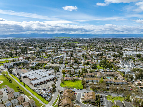 Drone images showcasing residential neighborhoods in Fremont, California, with lush green hills in the background and a mix of townhomes, single-family homes, and commercial buildings. Ideal for theme