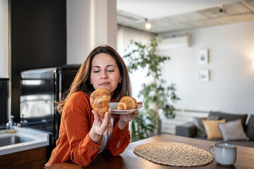 Woman holding croissant and plate at home in kitchen
