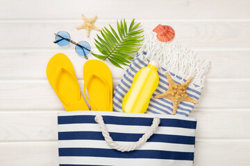 Blue beach bag with summer accessories on wooden background, top view