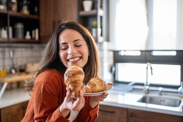 Happy woman enjoying freshly baked croissants in kitchen