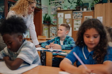 Elementary school pupils studying in classroom with teacher assisting