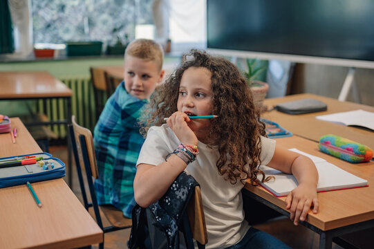 Thoughtful elementary school student chewing on pencil in classroom