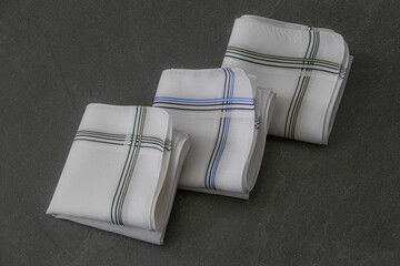 Classic men’s handkerchiefs with striped pattern on dark stone background.