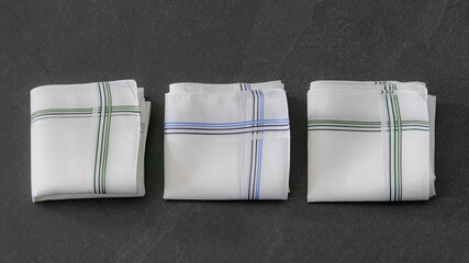 Classic men’s handkerchiefs with striped pattern on dark stone background.