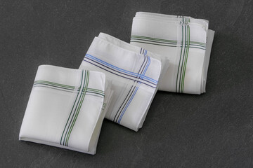 Classic men’s handkerchiefs with striped pattern on dark stone background.