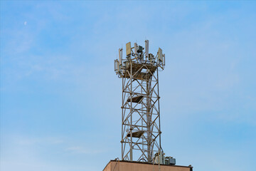 White antennas on a cell tower. A mobile data transmission tower installed on the roof of a building with antennas against a blue sky, telecommunications equipment, high-speed mobile communication.