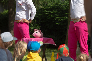 There are two individuals wearing bright pink pants standing close to a table that has an adorable stuffed pig sitting on it