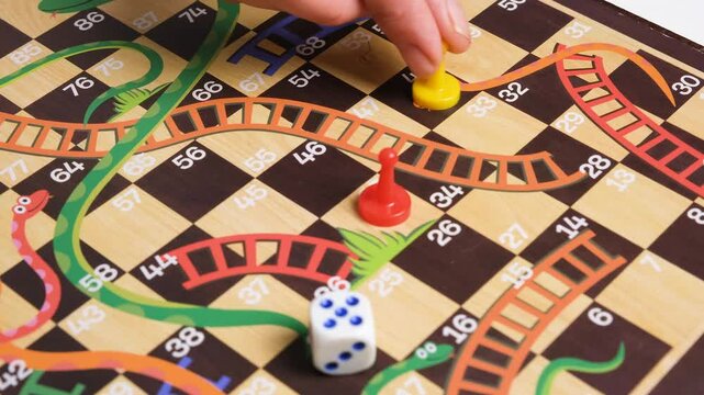 Hand moving yellow game piece on colorful board game table with dice and red pawn. Board game time with friends concept