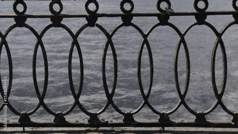 Poster a bird perched on a railing with water in the background, perfect for using as a peaceful scene or w