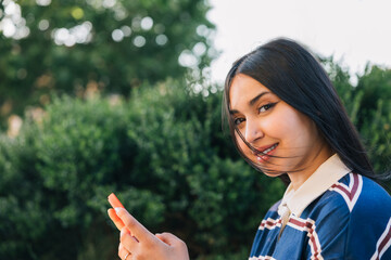 Smiling young woman using smartphone in park on breezy day. Lifestyle.