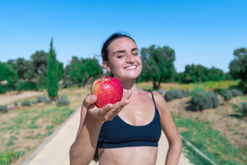 Mujer con una sonrisa ofreciendo una manzana roja con enfoque selectivo, un día soleado con cielo...