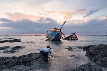 Old wrecked fishing boat at shore of Ang Sila Village, Chonburi Province of thailand with sunset skyline and clouds background. Include photographer to shoot for beautiful landscape at twilight.