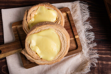 Close-up of two delicious cream-filled pastries, sprinkled with sugar, on a wooden board. Cuello...