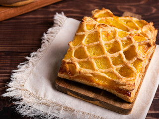 Two golden-brown pastries with a lattice crust and a vibrant yellow filling, rest on a wooden board