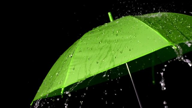 Closeup of rain hitting a green umbrella, water droplets splashing and sliding off in slow motion during a downpour

