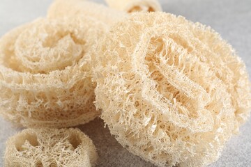 Different loofah sponges on light grey table, closeup