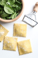 Uncooked ravioli, cutter and spinach on white table, flat lay