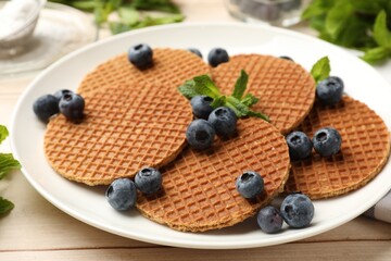 Tasty Dutch waffles (stroopwafels), mint and blueberries on light wooden table, closeup