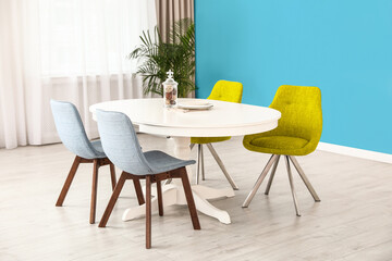 Dining table and colorful chairs near light blue wall in room. Interior design