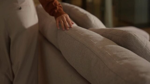Close-up of hand gently touching sofa backrest in warm and inviting living room