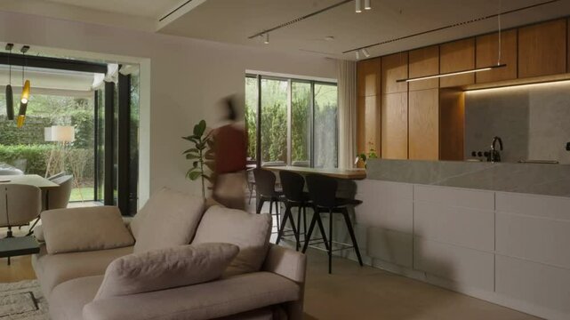 Modern kitchen and living space with person walking toward large glass doors to outside patio