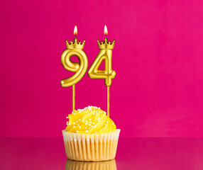 Yellow birthday cupcake with a number 94 candle - Birthday card on a pink background