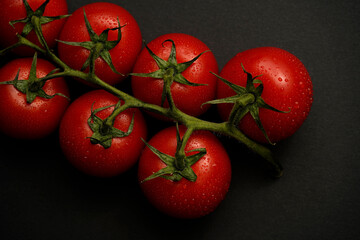 Fresh red tomatoes on a vine with water drops on a dark background. High contrast food photography showcasing natural freshness and organic quality. Perfect for advertising, healthy lifestyle content,