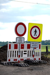 Road construction barricade with no entry and pedestrian crossing signs, placed on a gravel road...