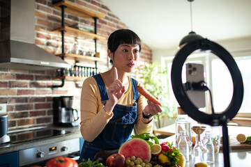 Woman filming healthy food vlog in kitchen with ring light and fresh produce