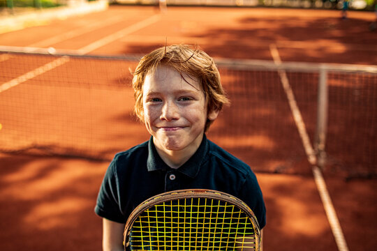 Portrait of a young boy smiling on a tennis court with a racket
