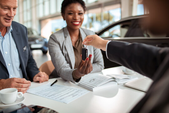 Happy diverse couple receiving car keys at dealership office