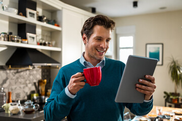 Young man using his digital tablet at home while drinking a cup of coffee