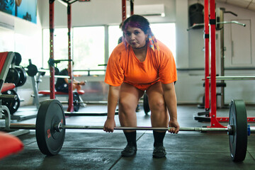 View of a beautiful, overweight young Latina lifting weights and working out at a gym. Positively, she's pushing herself to the limit. She's improving and feeling better.