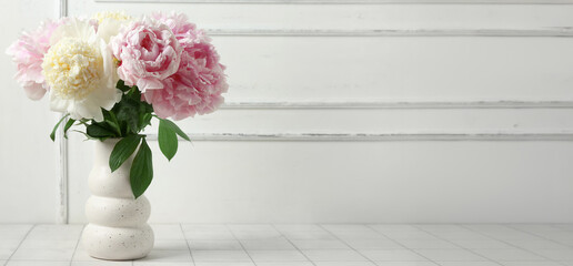 Vase with beautiful peony flowers on white tile table