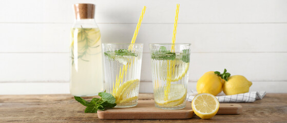 Glasses and bottle of fresh lemonade with mint on wooden table